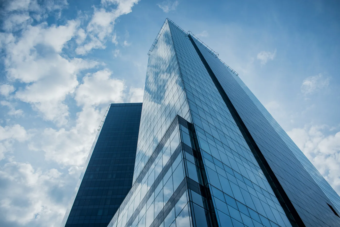 Glass skyscrapers seen from below against a blue sky with clouds