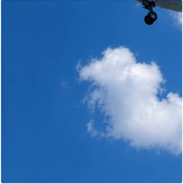 Tren de aterrizaje de un avión visto desde abajo contra un cielo azul con nubes