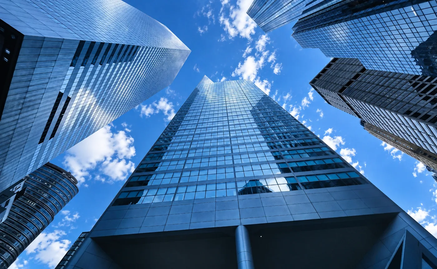 Glass skyscrapers seen from below against a blue sky with clouds