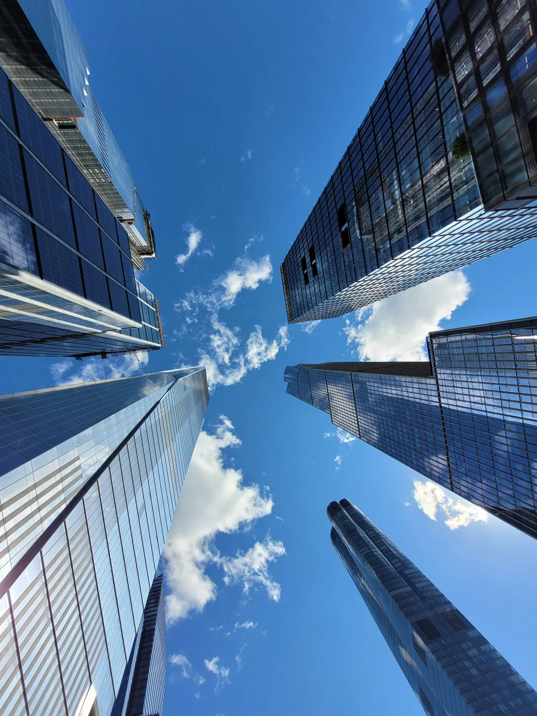 Glass skyscraper seen from below among other buildings against a blue sky