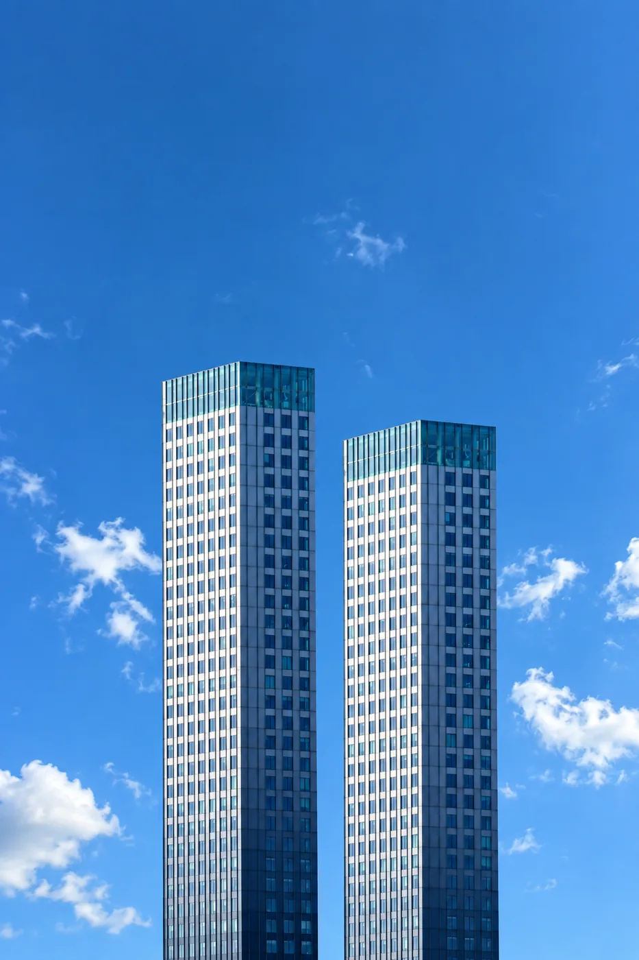 Two glass towers seen from below against a clear blue sky