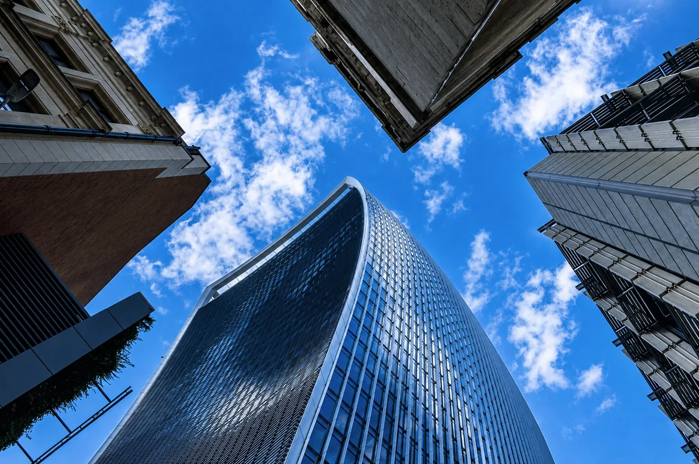 Rascacielos visto desde abajo entre otros edificios contra un cielo azul con nubes